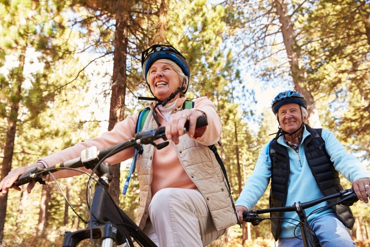 Two people on bikes in the woods smiling for a picture.